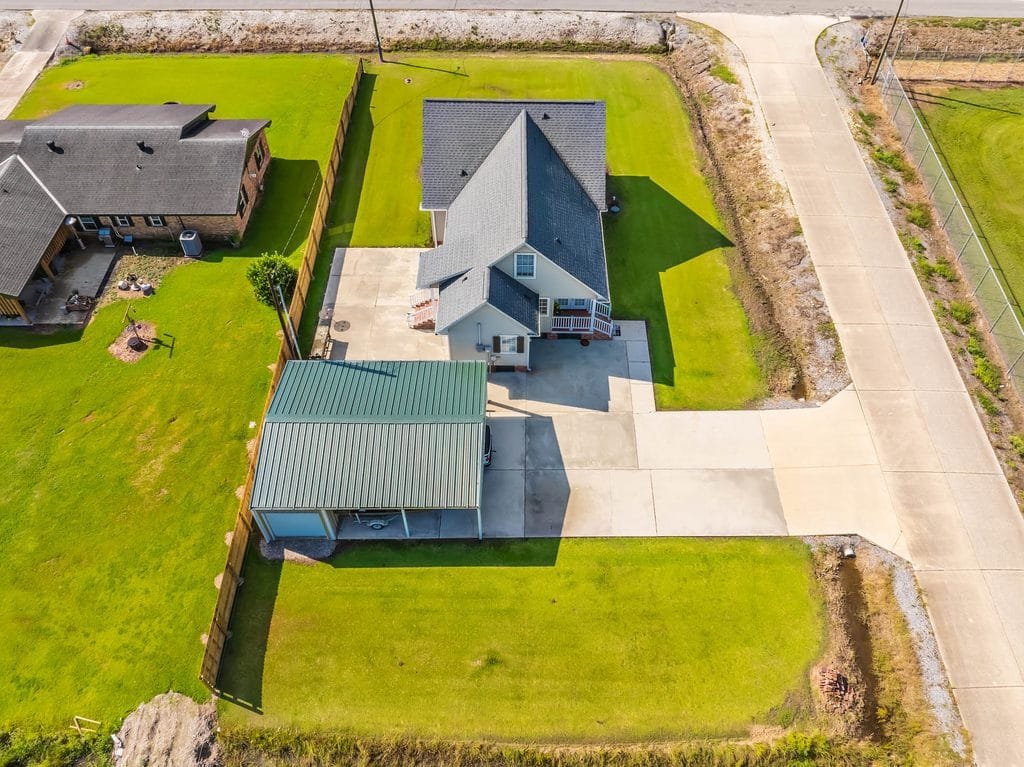 Aerial view of a house with a gray roof, driveway, covered carport, and green lawns, bordered by fences and roads on two sides—an excellent example for those seeking standout realtor photography examples.