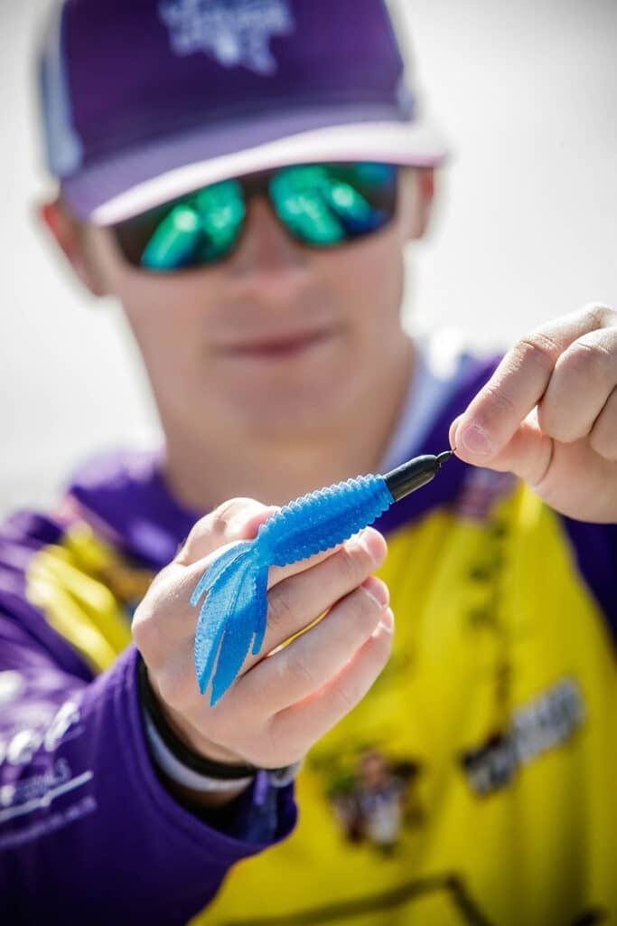CooperC_32_web A person in sunglasses and a purple and yellow shirt holds a blue fishing lure, focusing on attaching or displaying it with both hands—a perfect scene reminiscent of senior pictures with cars, trucks, hunting, and fishing themes.